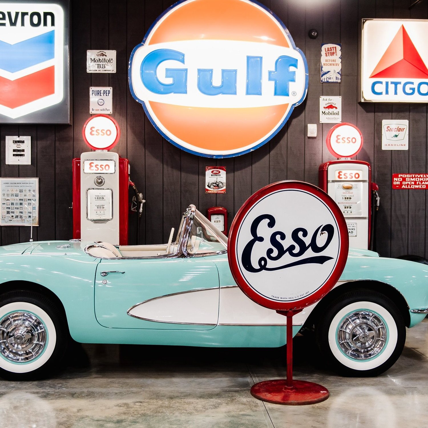 Vintage Gulf and Esso signs beside a turquoise convertible